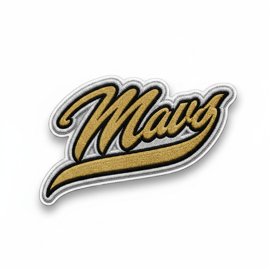 A die-cut embroidered patch featuring the word 'Mavs' in a stylized cursive script. The patch has a textured gold fill with black and white embroidered outlines, set against a gray and white checkerboard background.